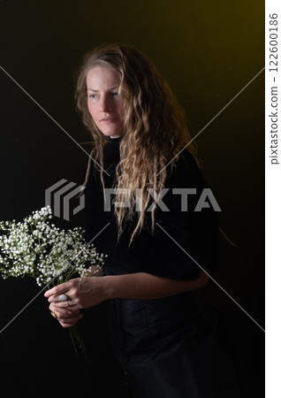 A beautiful mature woman holds a white flowers on a dark studio background. 122600186
