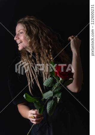 Beautiful young woman with single red rose flower on black studio background 122600231
