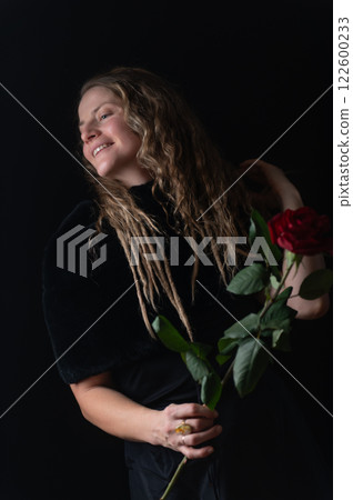 Beautiful young woman with single red rose flower on black studio background 122600233