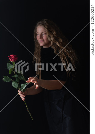 Beautiful young woman with single red rose flower on black studio background Beautiful young woman with single red rose flower on black studio background 122600234
