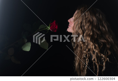 Beautiful young woman with single red rose flower on black studio background 122600304
