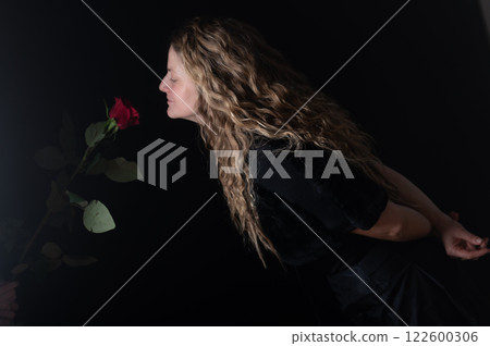 Beautiful young woman with single red rose flower on black studio background Beautiful young woman with single red rose flower on black studio background 122600306