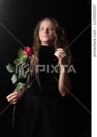 Beautiful young woman with single red rose flower on black studio background 122600307