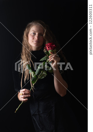 Beautiful young woman with single red rose flower on black studio background 122600311
