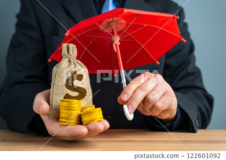 Businessman holding money bag with coins under red umbrella. Savings and deposits insurance concept. Capital preservation. 122601092
