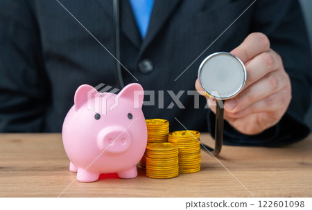 Businessman with stethoscope and piggy bank with coins. Financial health and well-being concept. Manage money wisely, ensure financial stability 122601098
