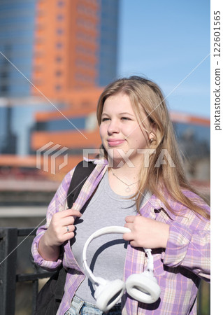 A young woman looks content while standing near a railing, the city behind her bathed in sunlight. The scene showcases the harmony of self-expression and urban exploration. A young woman looks content while standing near a railing, the city behind her bathed in sunlight. The scene showcases the harmony of self-expression and urban exploration. 122601565