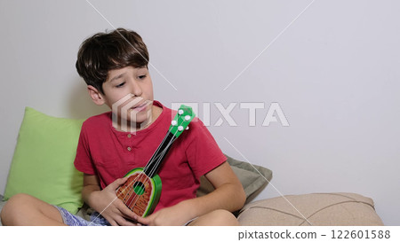 A young boy sits with a vibrant green toy guitar, showcasing his musical exploration and creative spirit. A young boy sits with a vibrant green toy guitar, showcasing his musical exploration and creative spirit. 122601588