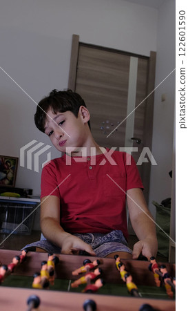 The boy actively plays table football, expressing genuine feelings and enthusiasm. The dynamic scene captures attention. 122601590