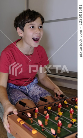 The boy is engrossed in table football, enjoying the game with an expressive look on his face. An emotional moment in play. 122601591