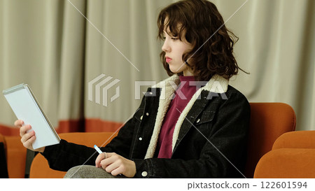 A girl playfully extends her notebook forward, her expression both focused and amusing. The photo highlights themes of creative problem-solving and lighthearted concentration. 122601594