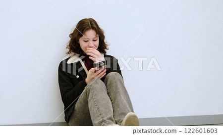 A cheerful girl with a playful expression reacts while using her phone. The photo reflects modern youth engagement with technology and the joy of staying connected digitally. 122601603