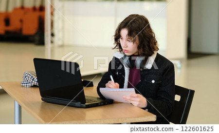 A girl immersed in her laptop studies in a spacious, bright room. This scene embodies the empowerment of young learners through technology and the shift toward virtual education. A girl immersed in her laptop studies in a spacious, bright room. This scene embodies the empowerment of young learners through technology and the shift toward virtual education. 122601625