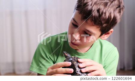 child looks intently at a small turtle resting in his hands, showing his gentle connection with his pet. This image highlights the bond between children and animals, representing care and curiosity. child looks intently at a small turtle resting in his hands, showing his gentle connection with his pet. This image highlights the bond between children and animals, representing care and curiosity. 122601694