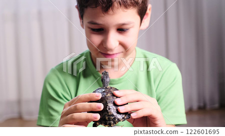 young boy holds a turtle gently, focused on the small reptile in his hands. This image reflects a moment of curiosity and care, representing the bond between children and pets. 122601695