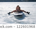 Happy brunette woman in swimsuit sitting on sup board posing looking at camera. 122601968