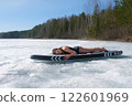 Woman in swimsuit basking in sun lying on sup board on frozen ice on river lake. 122601969