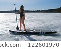 Woman in swimsuit posing smiling standing on sup board on frozen ice on river. 122601970