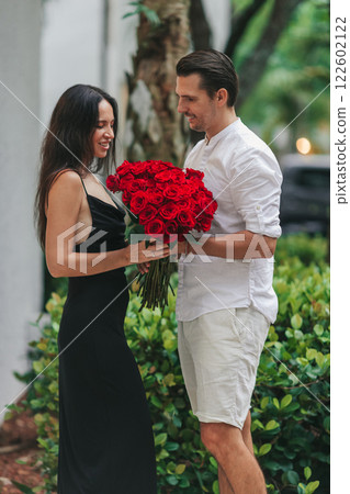 Young man gives his girlfriend a bouquet of red roses on Valentine's Day. The girl is wearing an elegant black dress. Valentine's Day Flowers 122602122