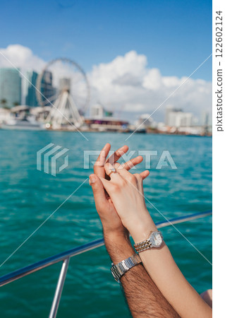 Close-up of a woman's hand with a diamond engagement ring against the backdrop of skyscrapers and a river Close-up of a woman's hand with a diamond engagement ring against the backdrop of skyscrapers and a river 122602124