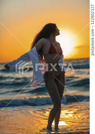 Adorable girl enjoying beautiful sunset on the beach, have fun splashing on the coast 122602127