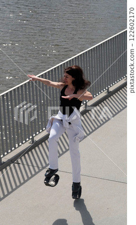 A woman in Kangoo Jumps boots moves energetically along a waterfront promenade, enjoying the outdoor workout. The rise of innovative fitness gear reflects the growing trend of fun and engaging 122602170