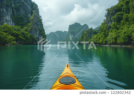 Orange kayak navigating tranquil emerald waters surrounded by lush limestone cliffs Orange kayak navigating tranquil emerald waters surrounded by lush limestone cliffs 122602342