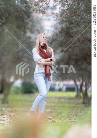 Young woman wearing scarf looking up at olive trees in park during autumn day 122602983