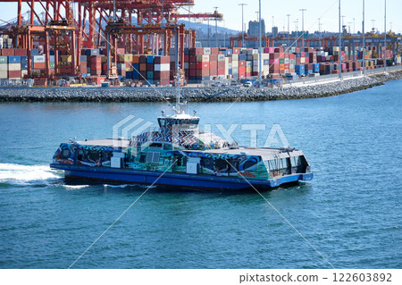 Canada Vancouver British Columbia Commercial harbor. Container Marine terminal with stacks of the boxes and operation management building. Ulusoy ferry boat on the water under blue sky Canada Vancouver British Columbia Commercial harbor. Container Marine terminal with stacks of the boxes and operation management building. Ulusoy ferry boat on the water under blue sky 122603892