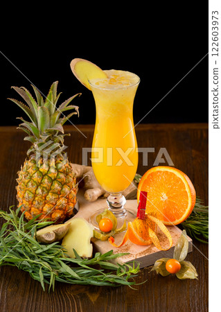 Closeup glass of fresh orange and pineapple juice decorated with ginger and fruits on a wooden table isolated at black background. Closeup glass of fresh orange and pineapple juice decorated with ginger and fruits on a wooden table isolated at black background. 122603973