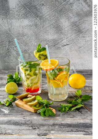 Two glasses of detox water with lemon, kiwi, orange and mint at concrete decorated table background. Concept of healthy lifestyle. 122603976