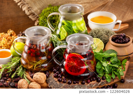 Three teapots with tea assortment decorated with nuts, citrus, black currant berries and mint at wooden table background. Three teapots with tea assortment decorated with nuts, citrus, black currant berries and mint at wooden table background. 122604026
