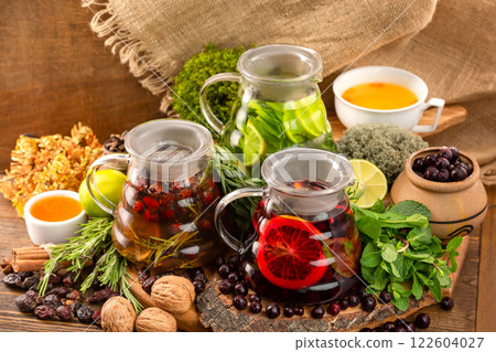 Three teapots with tea assortment decorated with nuts, citrus, black currant berries and mint at wooden table background. 122604027