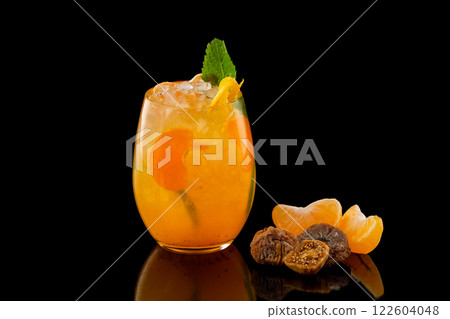 Closeup glass of orange tangerine fresh juice with ice cubes and a group of mandarin slices and figs isolated at black background. Closeup glass of orange tangerine fresh juice with ice cubes and a group of mandarin slices and figs isolated at black background. 122604048
