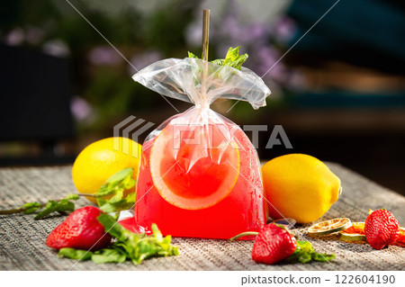 Red strawberry lemonade served in a plastic bag with lemons around at bar background. Red strawberry lemonade served in a plastic bag with lemons around at bar background. 122604190