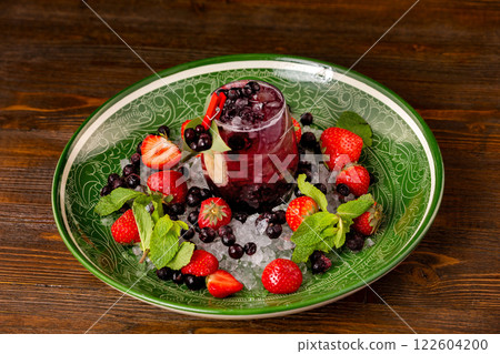 Black currant cocktail with berries and frappe at decorated with strawberry and mint plate at wooden table background. Black currant cocktail with berries and frappe at decorated with strawberry and mint plate at wooden table background. 122604200