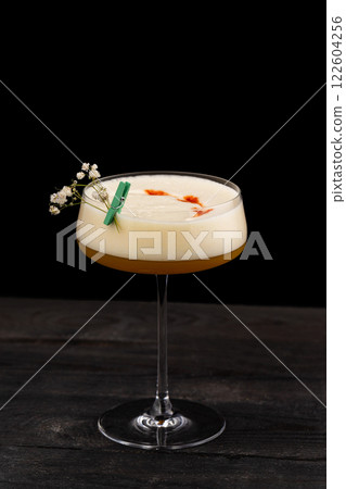 Closeup glass of cocktail with egg foam and white wine at wooden table isolated at black background. Closeup glass of cocktail with egg foam and white wine at wooden table isolated at black background. 122604256