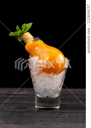 Closeup glass of cocktail with mango and pineapple juice and rum decorated with mint served in a lamp at wooden table isolated at black background. 122604257