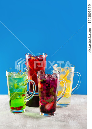 Group of lemonade jars with different ingredients and sorts of beverage at concrete textured table isolated at blue background. Group of lemonade jars with different ingredients and sorts of beverage at concrete textured table isolated at blue background. 122604259