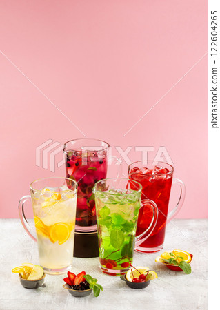 Group of lemonade jars with different ingredients and sorts of beverage at concrete textured table decorated with fruits and berries isolated at pink background. Group of lemonade jars with different ingredients and sorts of beverage at concrete textured table decorated with fruits and berries isolated at pink background. 122604265