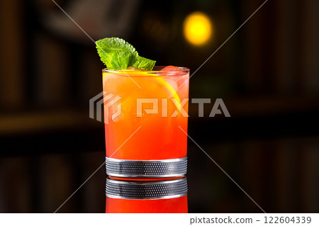Glass of tequilla sunrise cocktail decorated with mint at dark bar counter background. 122604339