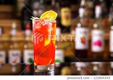 Closeup glass of cocktail with strawberry syrup, rum and lemon decorated with orange slice at bar background. 122604343