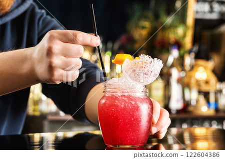 Bartender is decorating red cocktail in jar with frappe at bar counter background. Bartender is decorating red cocktail in jar with frappe at bar counter background. 122604386