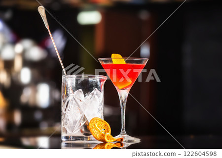 Closeup glass of Manhattan cocktail decorated with orange and decanter with ice at bar counter background. 122604598