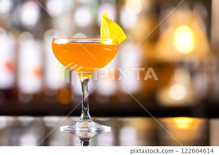 Glass of orange cocktail decorated with lemon at bar counter background. Glass of orange cocktail decorated with lemon at bar counter background. 122604614
