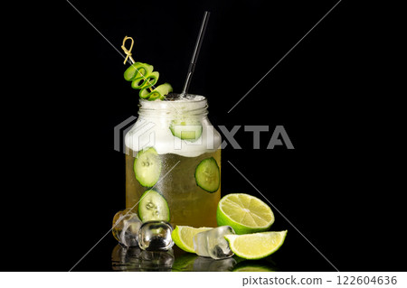 Closeup image of jar with cucumber cocktail decorated with lime isolated at black background. Closeup image of jar with cucumber cocktail decorated with lime isolated at black background. 122604636
