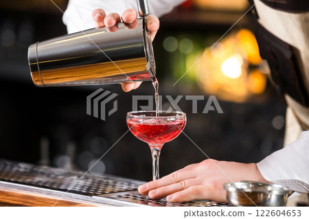 Male bartender is making cocktail pouring alchohol from shaker to glass at bar background. 122604653