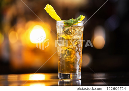 Closeup glass of long island ice tea cocktail decorated with mint at orange lighted bar counter background. 122604724