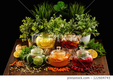 Set of colorful glass tea pots decorated with green plants and berries on a wooden table board at dark background. Set of colorful glass tea pots decorated with green plants and berries on a wooden table board at dark background. 122604743