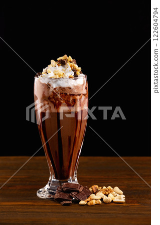 Closeup glass of chocolate milk shake with nuts decorated with whipped cream isolated at wooden board background. 122604794